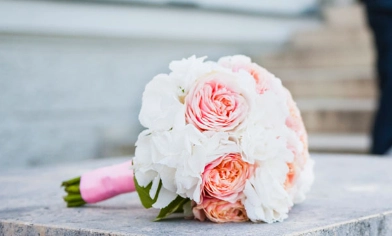 Wedding bouquet with pink and white roses, sat on stone stair bannister, bride & groom in distance